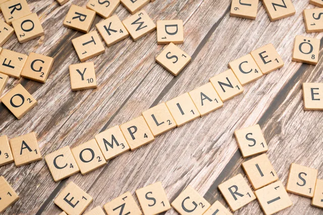 Wooden letter tiles forming the word 'COMPLIANCE' on a rustic wooden background. 4 moderation and records duties UK community teams must document